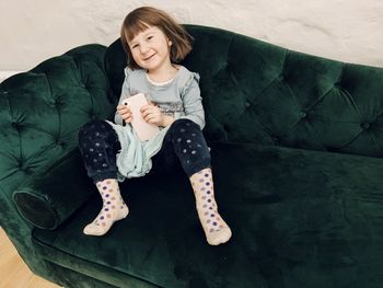 Toddler girl sitting on a green sofa with a pink smartphone in her hands