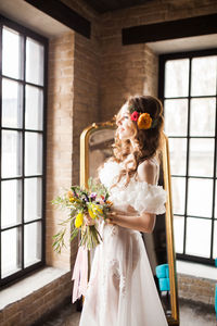 Woman holding flower bouquet against wall