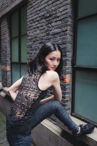 Portrait of beautiful young woman standing against brick wall