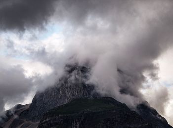 Low angle view of rocky mountain against cloudy sky