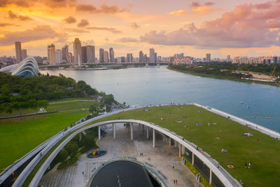 Green rooftop of marina barrage over river by buildings against sky during sunset