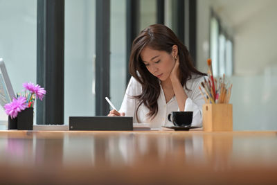 Young woman using phone while sitting on table