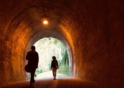 Rear view of silhouette people walking in illuminated tunnel