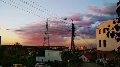Electricity pylon and buildings against sky during sunset