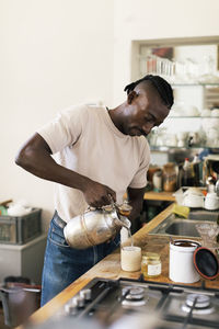 Businessman pouring water in cup while standing at workshop kitchen