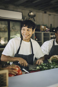 Smiling male seller cutting vegetable while working with colleagues in food truck