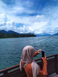 Woman in hijab photographing sea against sky