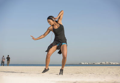 Woman listening music on headphones while dancing on sand at beach