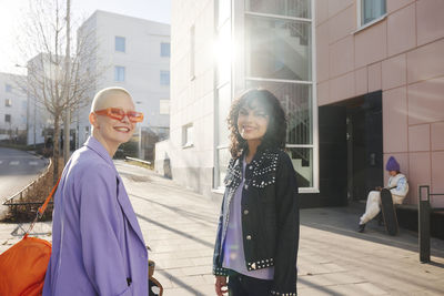 Smiling female friends or gay couple standing at road and looking at camera