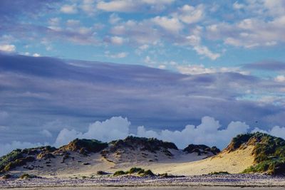 Sand dunes against cloudy sky