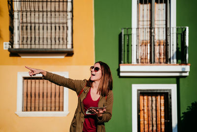 Smiling woman with map standing against wall during sunny day