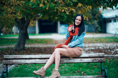 Portrait of young woman sitting on bench in park