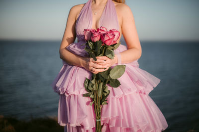 Midsection of woman holding pink while standing against sea