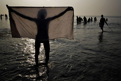 Silhouette man with textile standing against crowd at beach