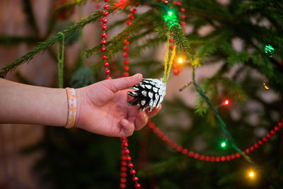 Cropped hand of child holding pine cone in illuminated christmas tree