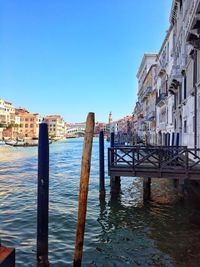 Wooden post in canal by buildings against clear blue sky