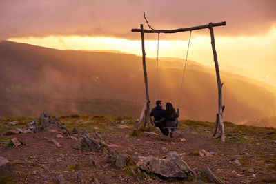 Rear view of men standing on mountain against sky during sunset