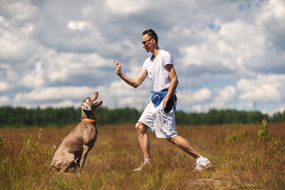 Man with dog on field against sky