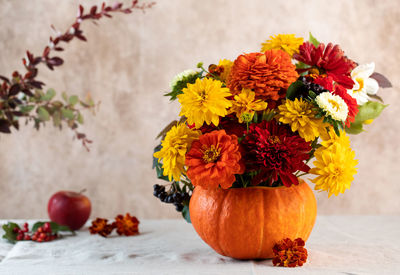 Bouquet of fresh flowers in pumpkin on table near beige wall