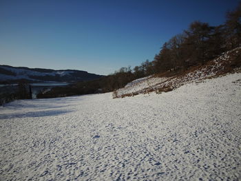 Surface level of snow covered land against clear blue sky