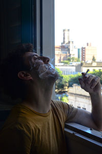 Portrait of man smoking against window