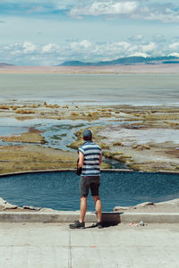 Rear view of man standing on sea shore against sky