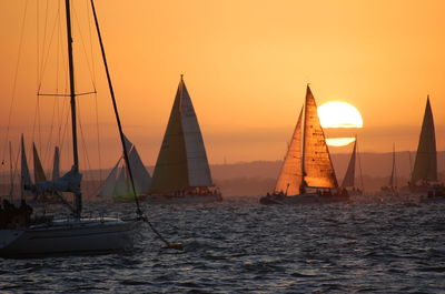 Sailboats sailing in sea against orange sky