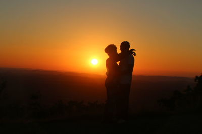 Couple embracing on field against sky during sunset