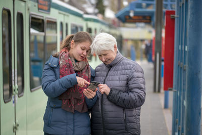 Grandmother and granddaughter using mobile phone at railroad station platform