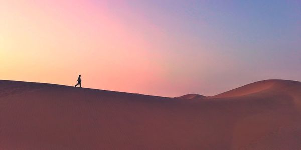 Silhouette person standing on desert against sky during sunset