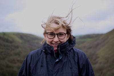 Portrait of smiling woman with tousled hair standing on mountain against sky