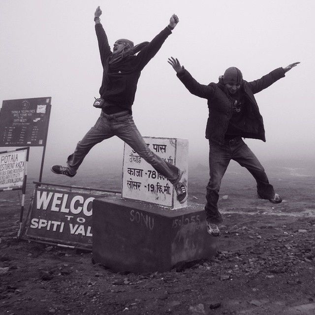 full length, lifestyles, leisure activity, jumping, mid-air, text, arms raised, enjoyment, fun, men, casual clothing, communication, western script, standing, arms outstretched, sky, human representation, sport