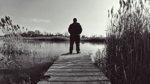 Rear view of man standing on pier against lake