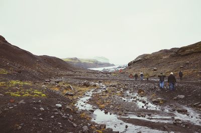 Rear view of people walking on mountain road against sky
