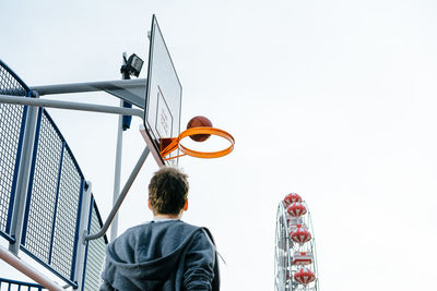 Rear view of man playing basketball on court against clear sky