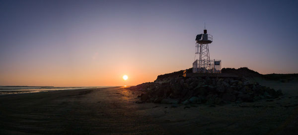 Lighthouse on beach against sky during sunset