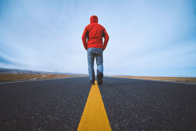 Rear view of man walking on road against sky