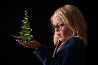 Digital composite image of cute girl with christmas tree on palm against black background