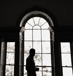 Silhouette woman looking through window in building