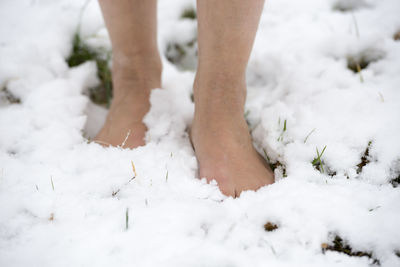 Low section of woman walking with barefoot on snow
