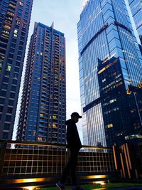 Low angle view of silhouette man standing by modern buildings in city against sky