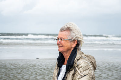 Senior woman standing at beach against sky