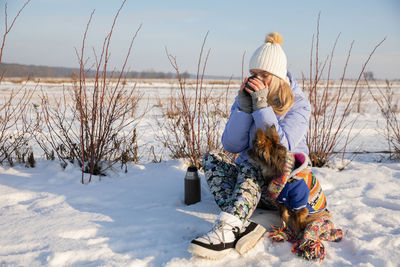 Rear view of woman sitting on snow covered field