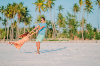 Full length of father playing with daughter against palm trees