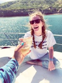 Cropped hand toasting drink with female friend on boat