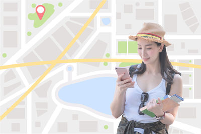 Young woman using mobile phone while standing against wall