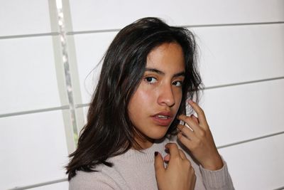 Portrait of young woman holding hair against wall
