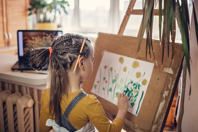 Rear view of girl painting at home