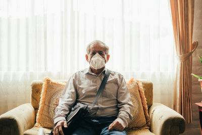 Portrait of man wearing mask sitting on sofa at home