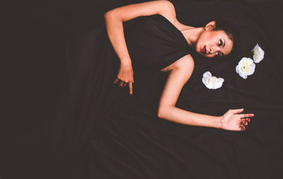 High angle view of young woman wearing black dress while lying with white flowers